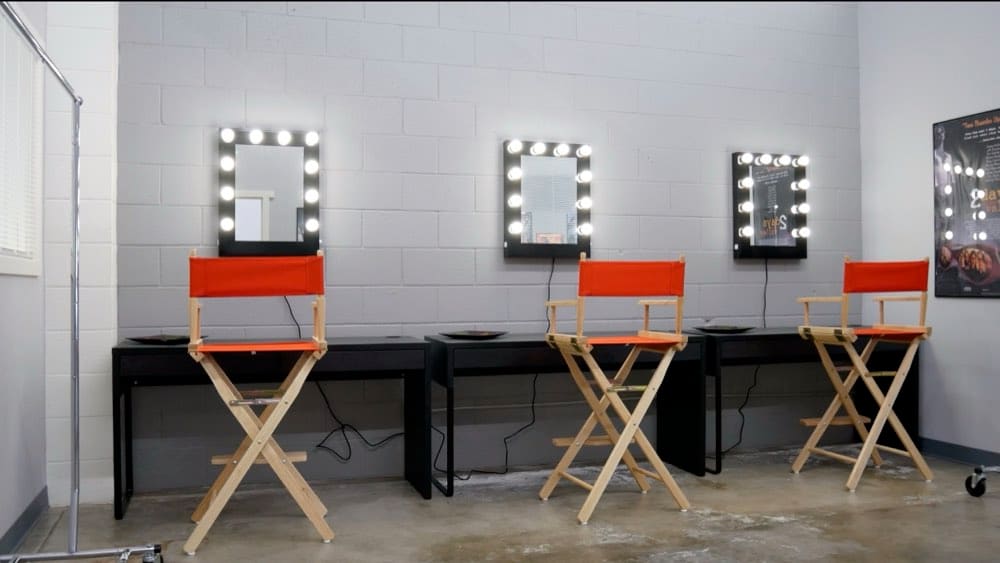 The hair and makeup room at the Burbank TV studio, with lit vanity mirrors and director's chairs