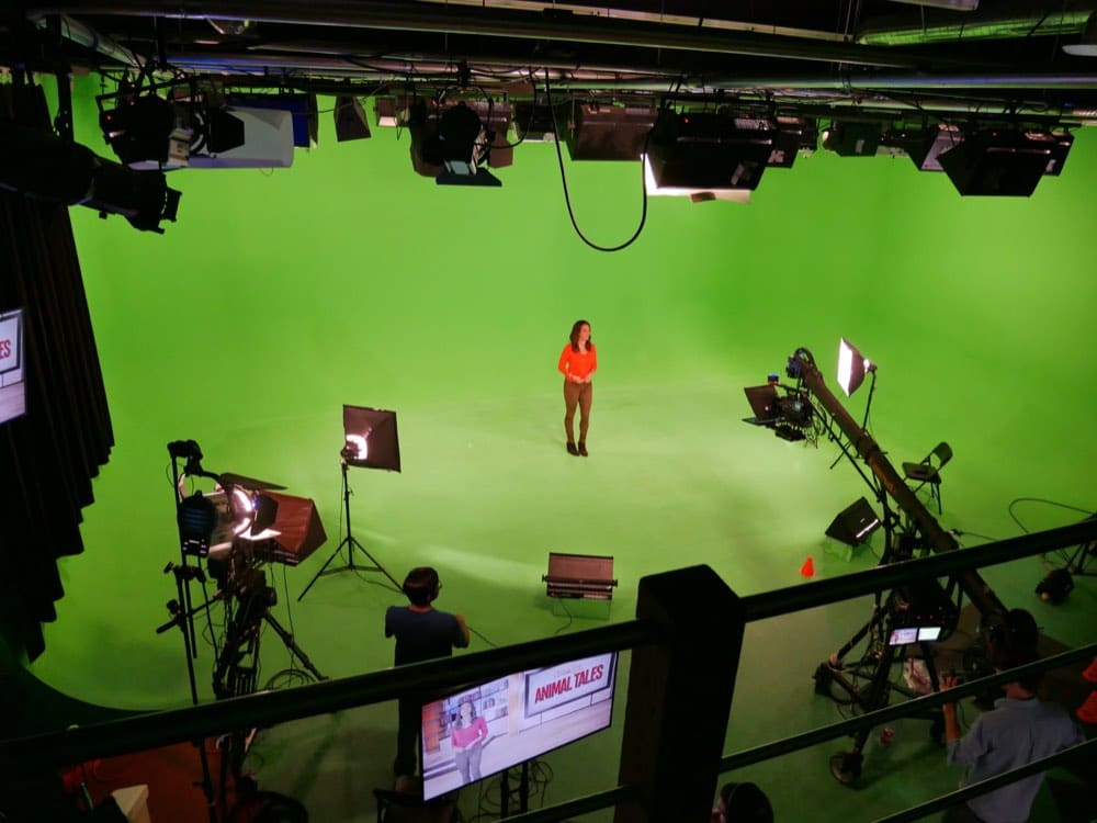The green-screen cyclorama at the Burbank stage seen from above: a presenter on the cyc under the lighting grid, with a camera crane and the live composite on the monitor below