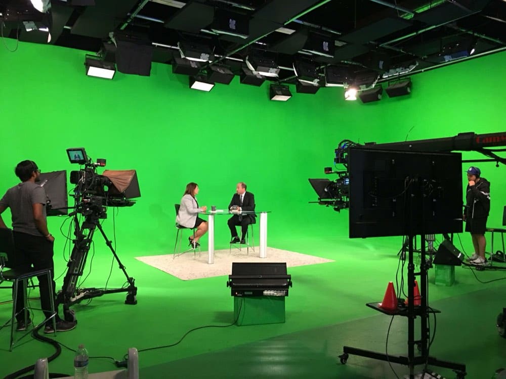 A two-camera interview setup on the Burbank virtual production stage, with crew, teleprompters and a full overhead lighting grid