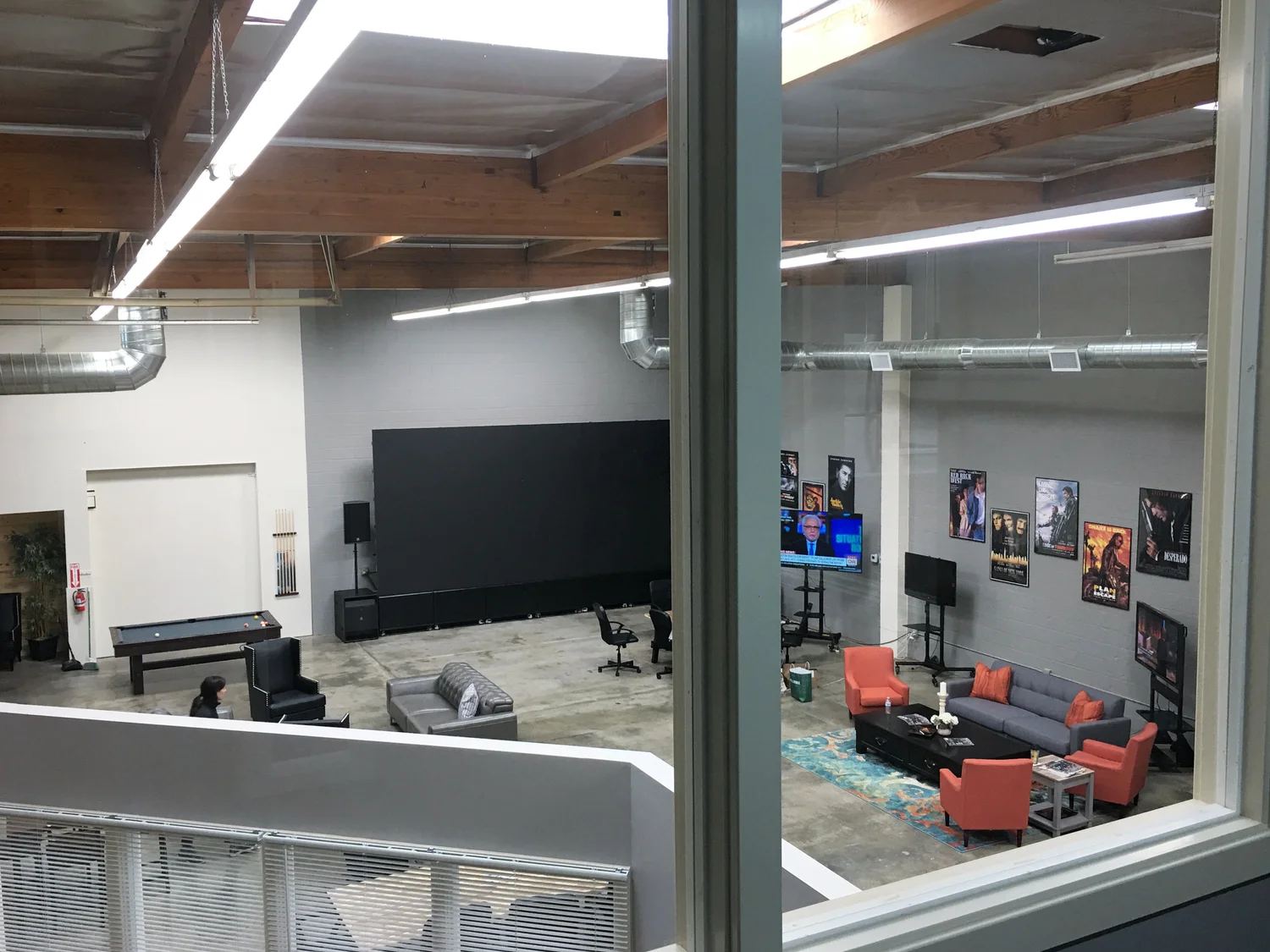 View over the Burbank production-office common area showing the in-house movie screen, a grand piano, and lounge seating.