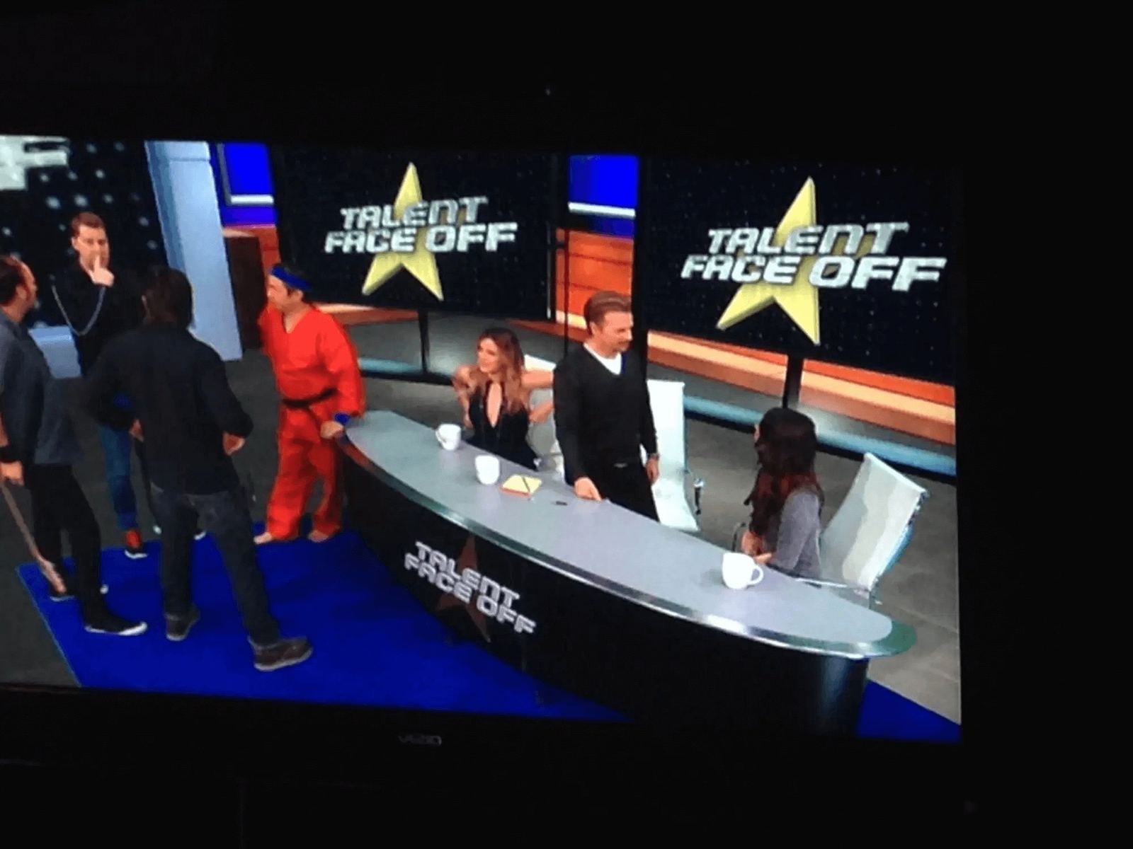 Game show set — 'Talent Face Off' judges at a desk with a contestant in a red jumpsuit, composited virtual production at L.A. & ABQ Castle Studios