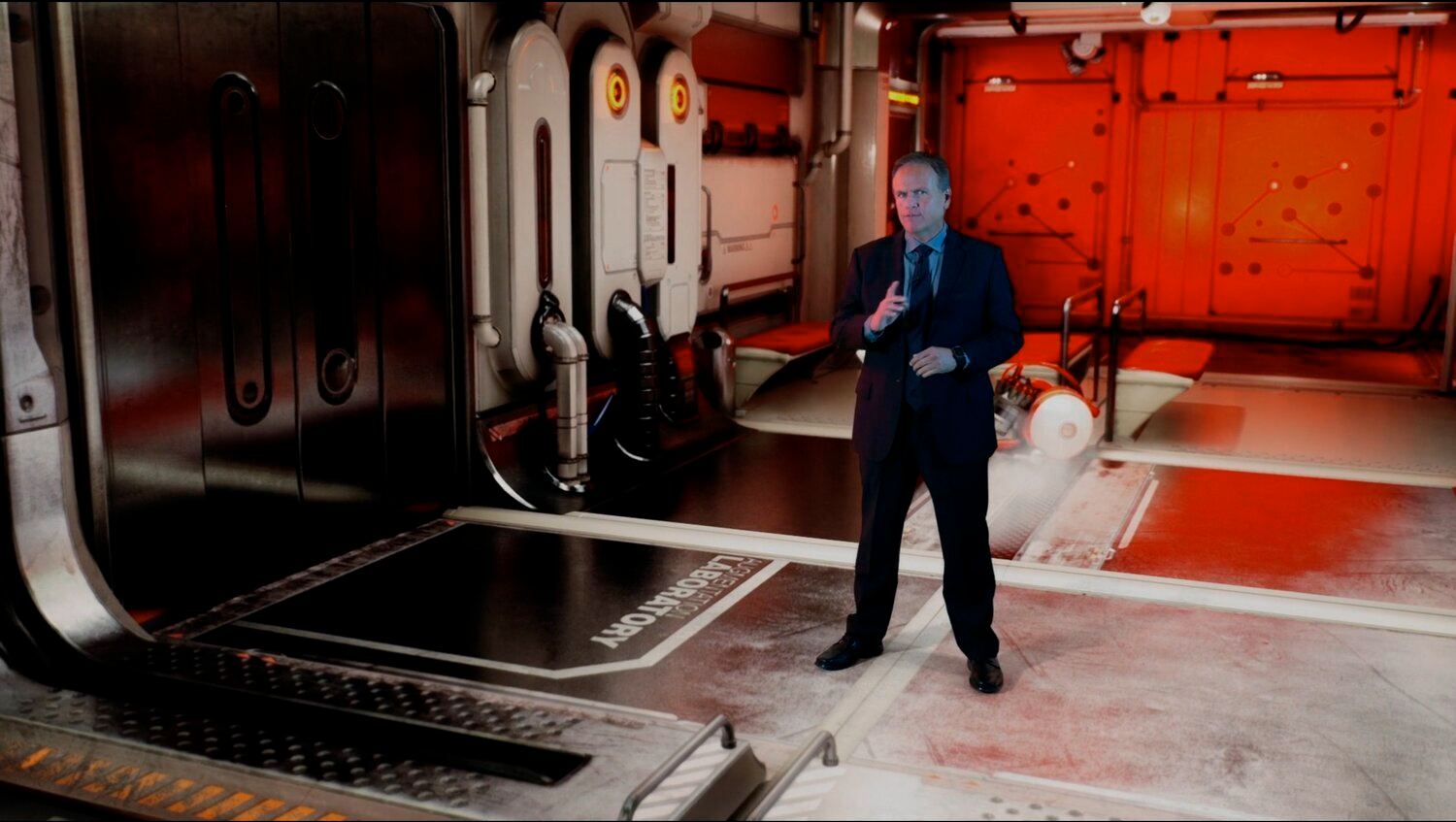 Space and sci-fi set — an actor in a suit stands in a red-lit spaceship laboratory corridor, an Unreal Engine virtual production set at L.A. & ABQ Castle Studios