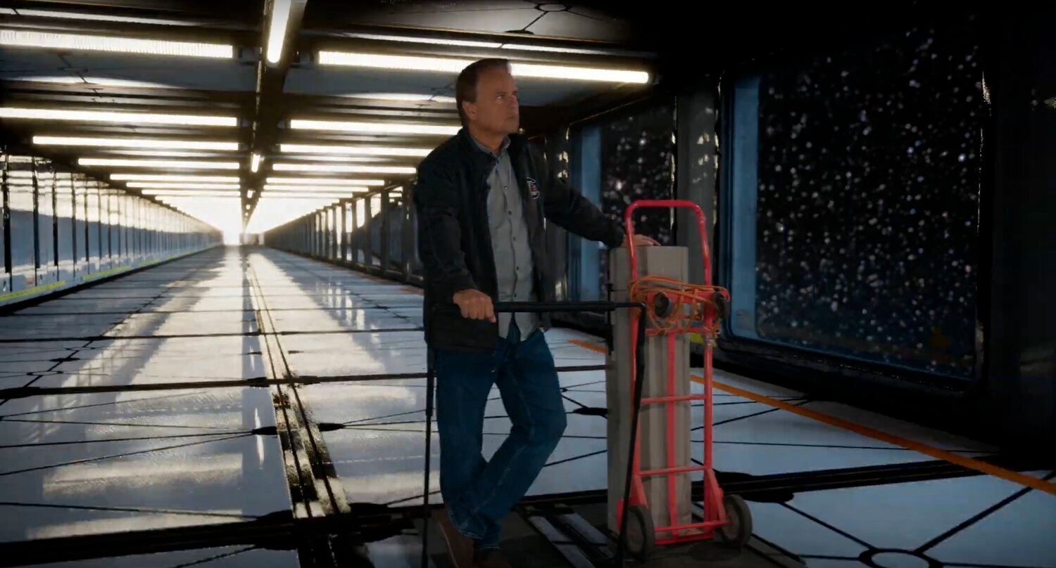 Space and sci-fi set — a man with a hand truck in a long glass-walled space corridor overlooking a starfield, an Unreal Engine virtual production set at L.A. & ABQ Castle Studios