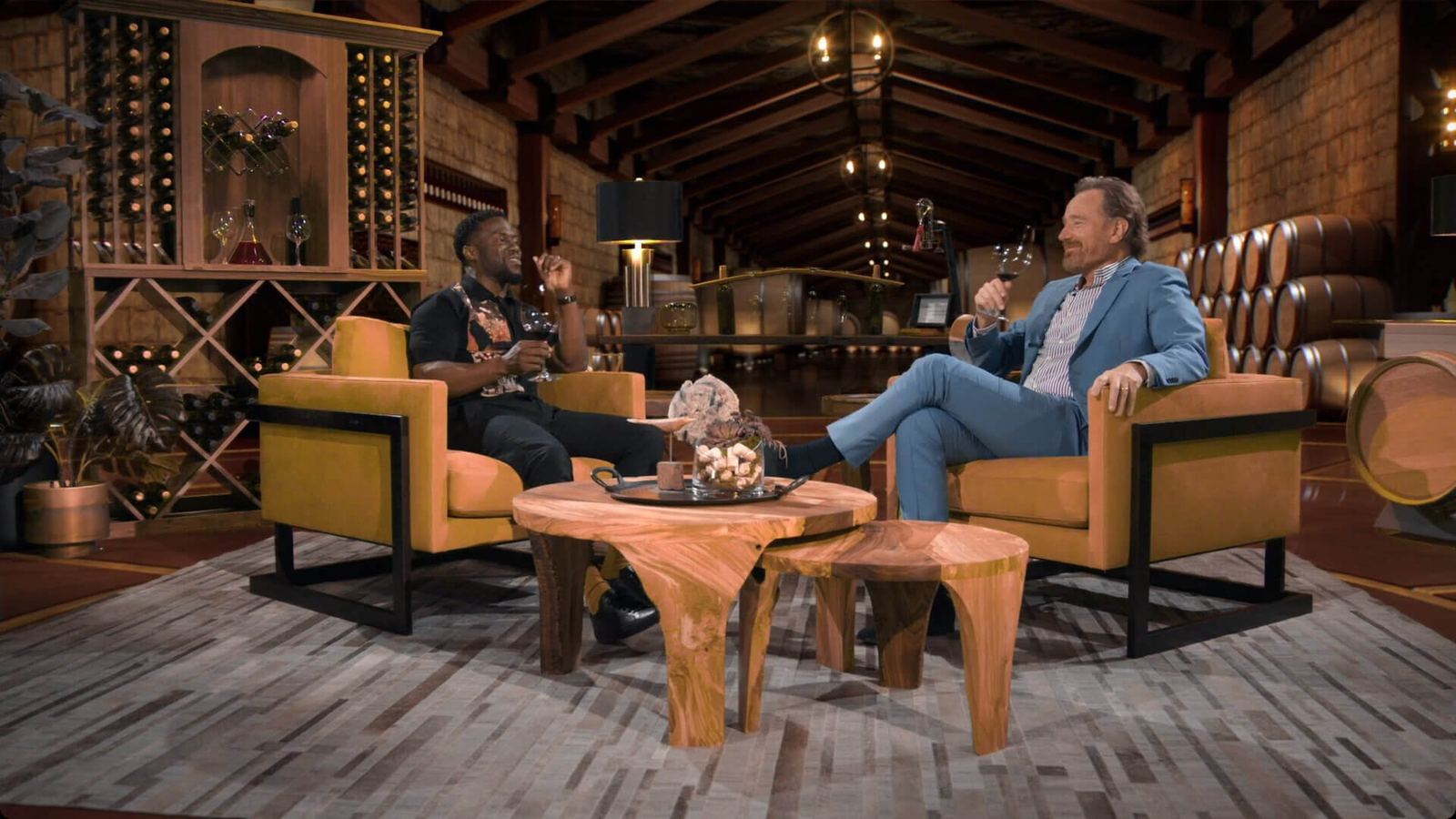 Talk show set — host and guest laughing with wine glasses in gold armchairs inside a virtual winery cellar, a virtual production set at L.A. & ABQ Castle Studios