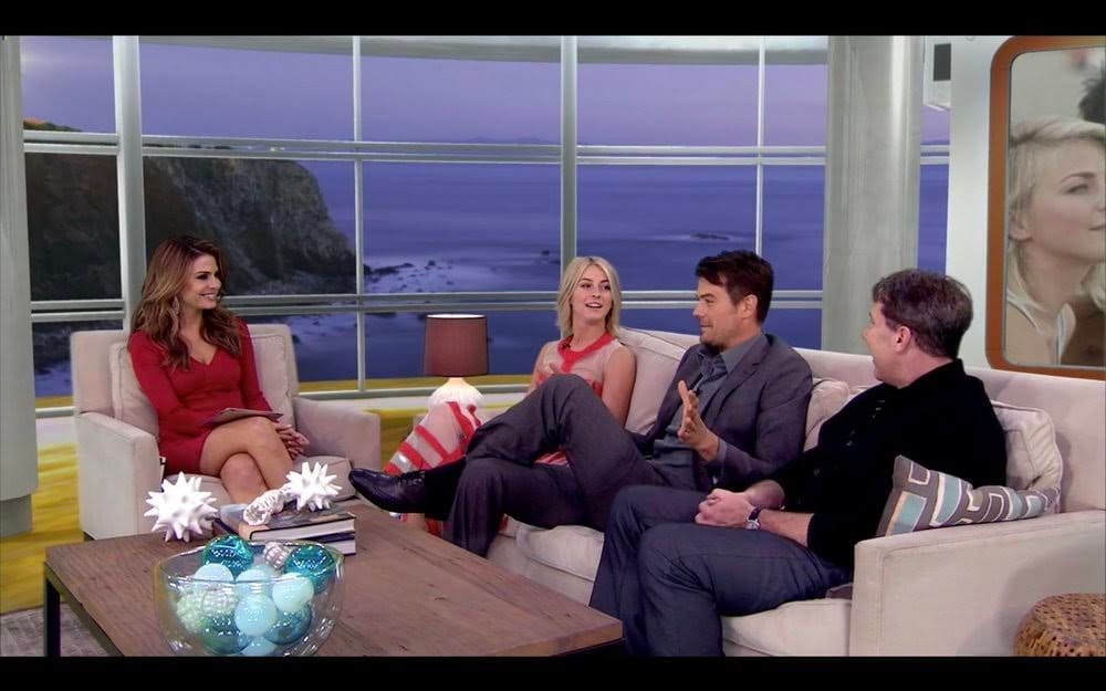 Talk show set — host and three guests on white sofas before a wraparound ocean-cliff window view at dusk, a virtual production set at L.A. & ABQ Castle Studios