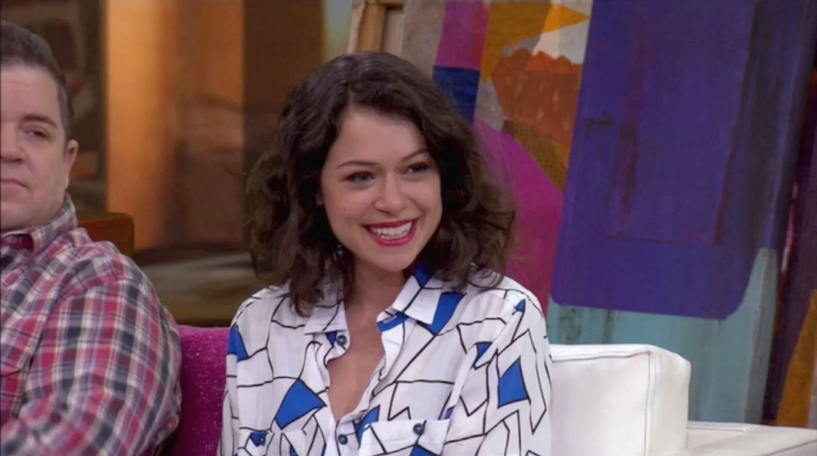 Talk show set — a smiling guest in a patterned blouse on a white couch before a colorful abstract art backdrop at L.A. & ABQ Castle Studios
