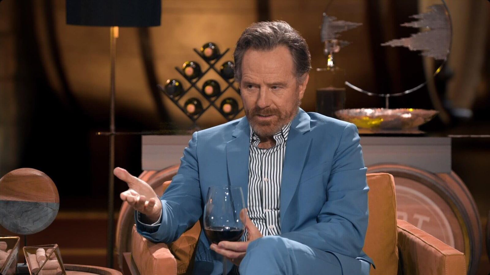 TV and film set — an actor in a blue blazer gestures with red wine in a warm wine-cellar lounge, a virtual production set at L.A. & ABQ Castle Studios