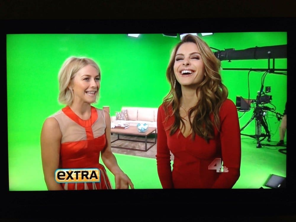 Virtual production studio — two laughing presenters on an 'Extra' couch segment on a green screen stage with a camera crane at L.A. & ABQ Castle Studios